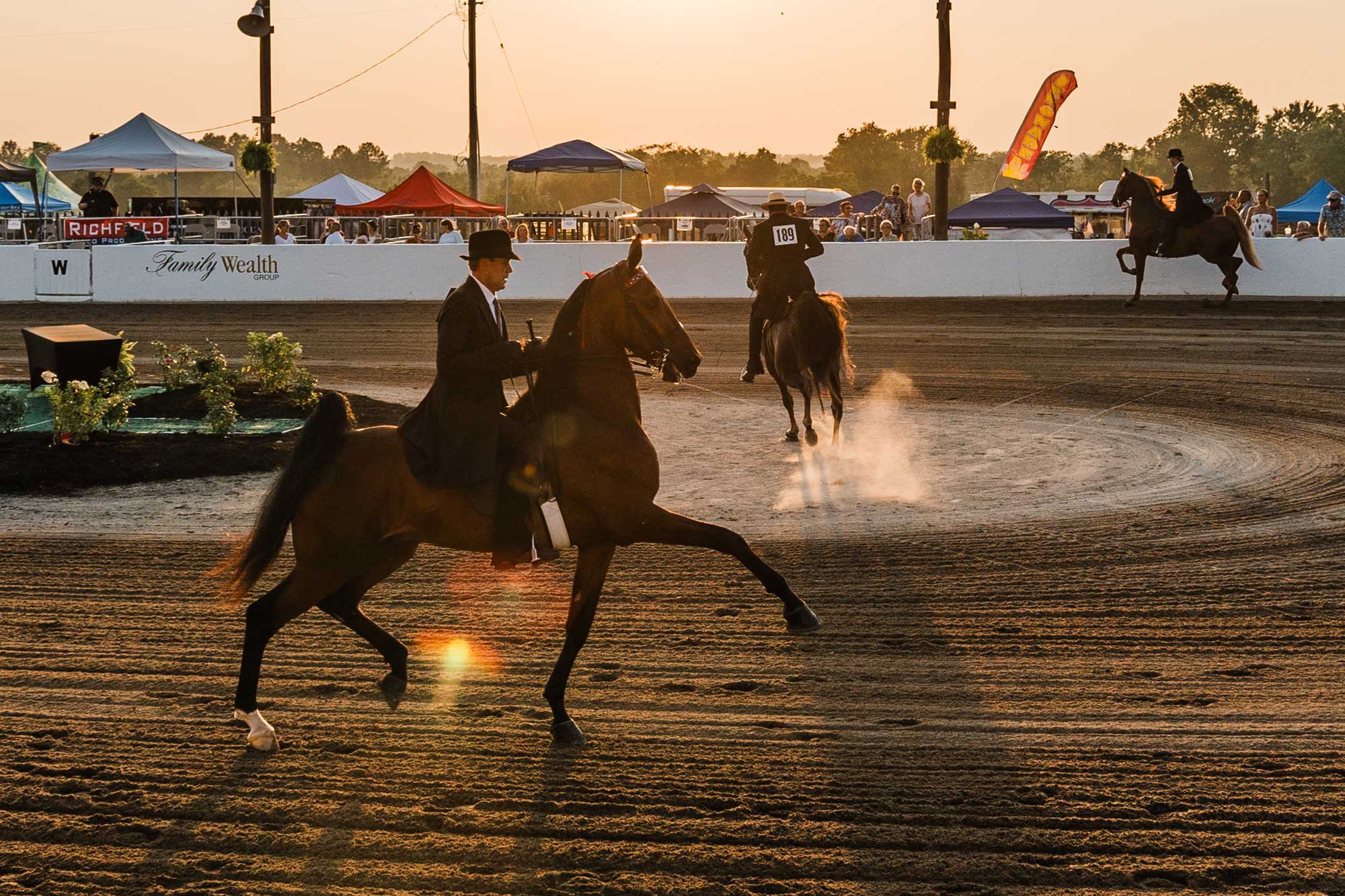 Riders on horseback circling fairgrounds track.