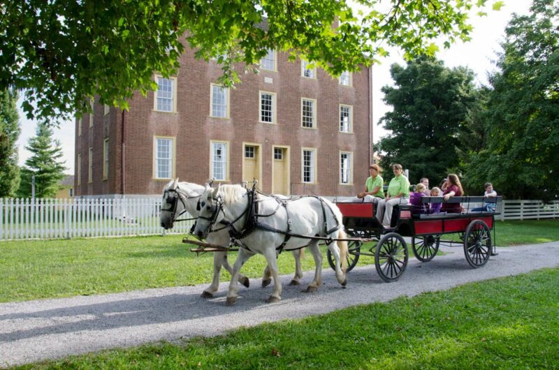 people in a horse-drawn wagon in front of a historic building.