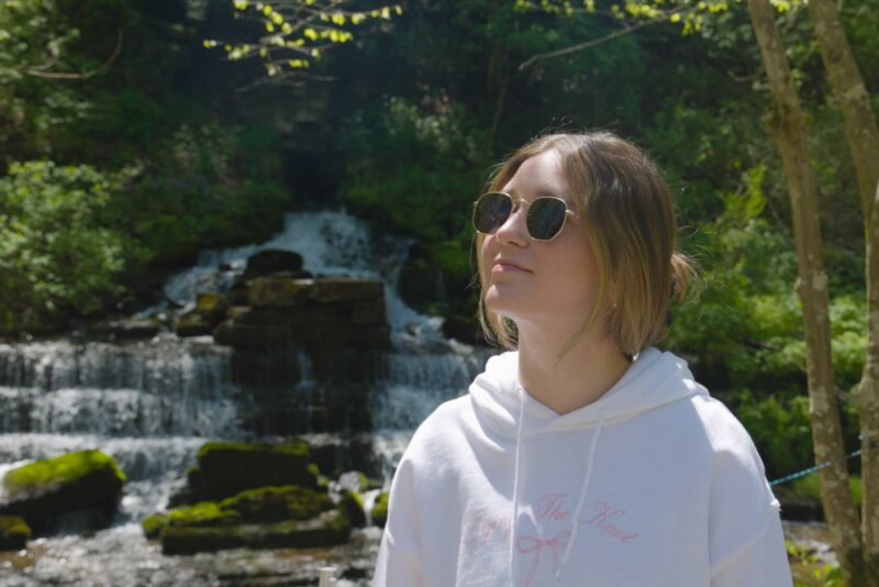 Young woman under trees with waterfall in background